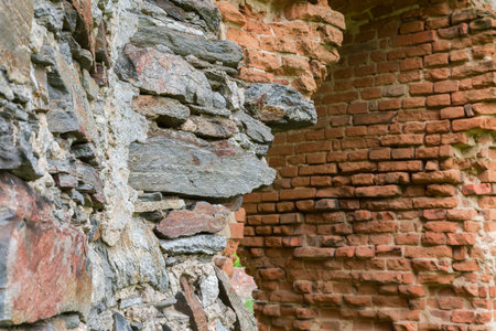 Fragment of the old defense structure built of stone and red brick in ruined medieval castle in spring overcast day, view close-up in selective focusの写真素材