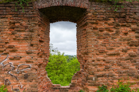 Fragment of the defense red brick structure with window opening of ruined medieval castle in spring overcast day, view from the courtyard sideの写真素材