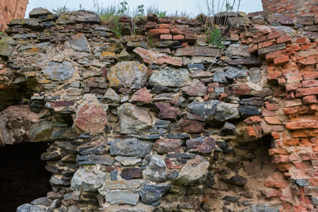 Fragment of the defense structure built of stones and red bricks in ruined medieval castle in spring overcast day, view from the courtyard sideの写真素材