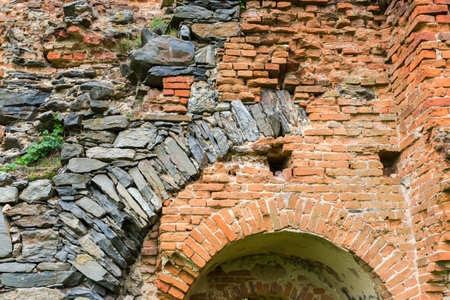 Fragment of the old defense structure built of stones and red bricks in ruined medieval castle in spring overcast day, view from the courtyard sideの写真素材