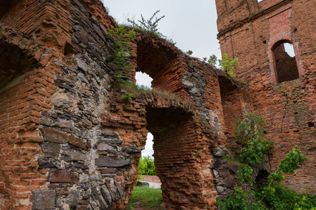 Fragment of the old defense wall and other structures built of stone and red brick in ruined medieval castle in spring overcast day, view from the courtyard sideの写真素材