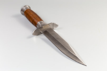 Non-folding hunting knife with forged steel pointed blade and wooden stained oak handle on a gray background, view close-up in selective focusの写真素材