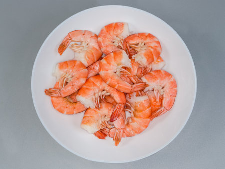 Freshly boiled unpeeled tails of the king prawns in their shells on the white dish, top view on a gray surfaceの写真素材