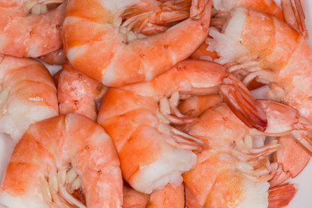 Small heap of freshly boiled unpeeled tails of the king prawns in their shells on the white dish, top view close-up in selective focusの写真素材