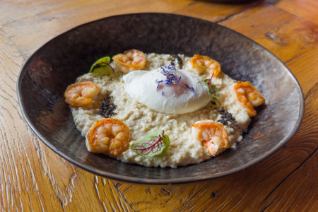 Breakfast of poached egg served with oat porridge and grilled prawn tails on the dark dish on an old...