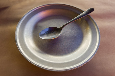 Empty old wide shallow metal aluminum plate with stainless steel spoon on table covered with kraft paper tableclothの写真素材
