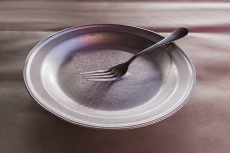 Empty old wide shallow metal aluminum plate with stainless steel fork on table covered with kraft...