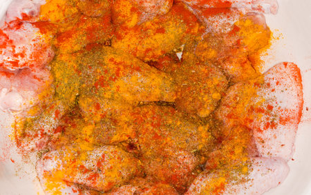 Raw chicken wings generously sprinkled with different spices in the white kitchen bowl for marinating before following grilling, top view close-upの写真素材
