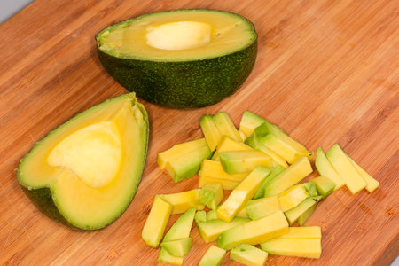Diced avocado, whole half and quarter of avocado with dark green skin on a wooden bamboo cutting...