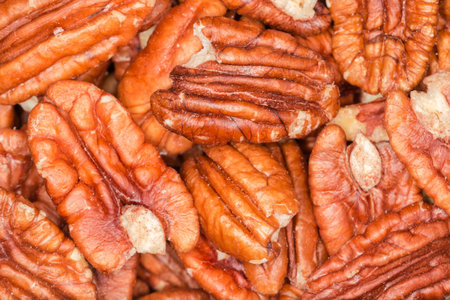 Small heap of the dried shelled pecan nuts, top view close-up in selective focus, background