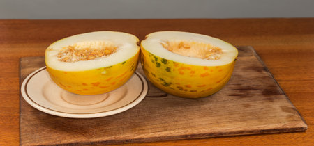 Round yellow melon with seeds cut in half on dish and on an old wooden cutting board on a wooden...