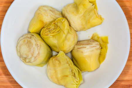 Canned heads of green artichoke in a white bowl on a wooden cutting board, top view close-upの写真素材