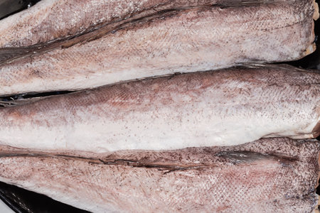 Uncooked defrosted carcasses of European hake without the heads and tails on a plate, top view of fragment close-upの写真素材