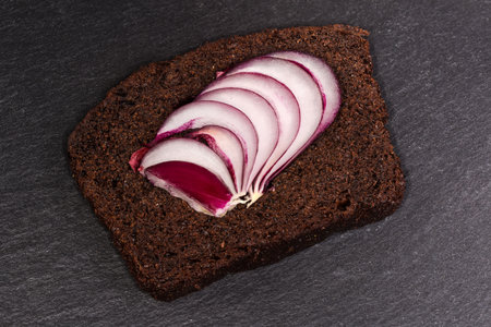 Slices of red sweet onion on a brown bread piece, as a sandwich blank on a black flat slate plate...