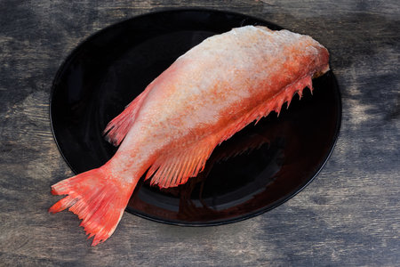 Raw defrosted gutted carcass of redfish, also known as ocean perch, without head on the big black plate on a black wooden surfaceの写真素材