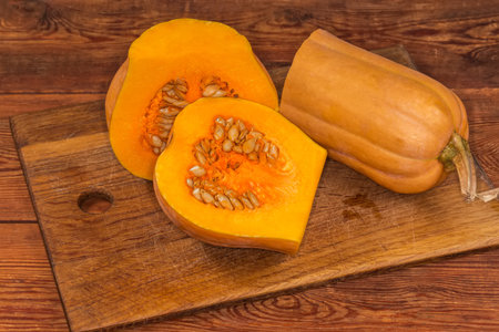 Orange butternut squash cut into three parts on a wooden cutting board on an old rustic tableの写真素材