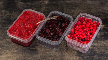 Macerated, dried and frozen cranberry in three open small plastic transparent food containers on black wooden rustic tableの写真素材