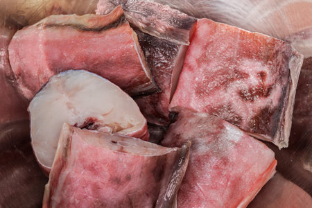Raw pieces of kingklip, also known as pink cusk-eel in a stainless steel kitchen bowl, top view...