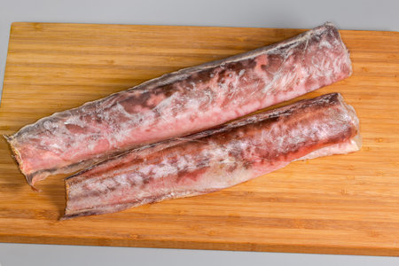 Two frozen carcasses of pink cusk-eel without of heads and tails covered with hoarfrost on a wooden...