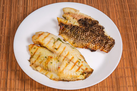 Two dourade boneless fillets on a skin grilled with spices served on a white plate on a table...