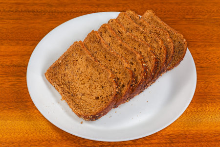 Slices of the rectangular loaf of cereal wheat-rye brown bread with various seeds on a white plate...