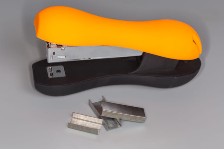Manual mechanical paper stapler with orange and black plastic anti-slip rubberized housing oval...