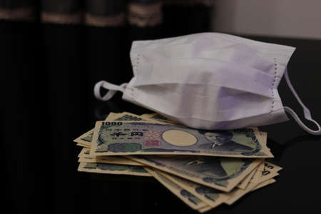 Japanese money and white mask placed on the tableの写真素材