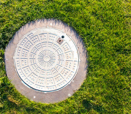 Metal manhole in a background of green grass on the field.の写真素材