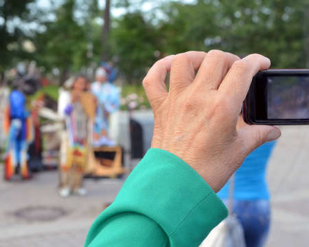 Hand of an elderly woman, who take video about street musicians with a mobile phone. musicians on background are blur.の写真素材