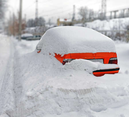Bright red car in a snowdrift skidded by snow on the parking after a heavy snowfallの写真素材