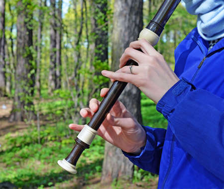 Fragment of  plastic recorder and hand of the young woman  flutist. She plays in the clear sunny day...