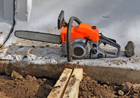 The chainsaw covered with sawdust at the bottom of a concrete wall fencing the building siteの写真素材