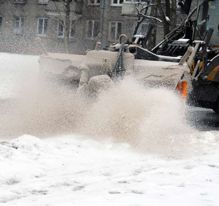 The rotating brush of the snowplow raises a cloud mixed snow and sand during cleaning of the street