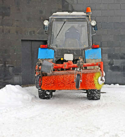 Short break in work on cleaning of snow in snowfall. Snowplow stands near dark wall. Back of tired...