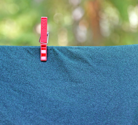 Red plastic clothespin fixes wet washed fabric on clothesline outdoor. Image can be used as background.の写真素材