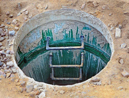 Open manhole of city sewage system with ladder leading down into underground communications on...