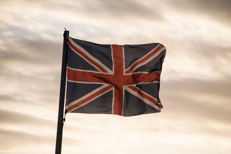 A Union Jack flag gently blowing in the wind agains a sunset