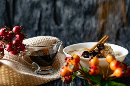 Sour-milk yogurt dessert, with thermostatic cooking, decorated with ripe cherry berries in syrup, on a dark background with jam in sauce and a stick of cinnamon, next to sprigs of fresh red berriesの写真素材