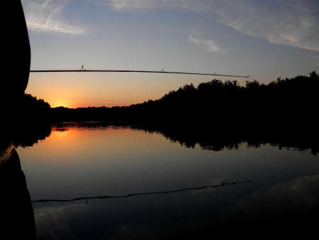 a fishing rod and a boat at sunset