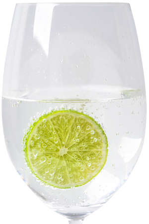 Close-up of a lime slice in sparkling soda water in a tall clear wine glass on white backgroundの写真素材