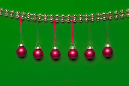 Six small matte red-coloured Christmas ornaments hanging on a row decorated by shiny golden-coloured...