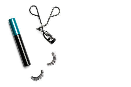 A closed bottle of mascara with a black body and blue-green cap, black steel eyelash curler, and 2 long dramatic false eyelashes arranged on the left side on white background shot with studio lightの写真素材