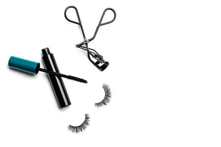 An open bottle of mascara with a black body and blue-green cap, black steel eyelash curler, and 2 long dramatic false eyelashes arranged on the left side on white background shot with studio lightの写真素材