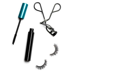 An open bottle of mascara with a black body and blue-green cap, black steel eyelash curler, and 2 long dramatic false eyelashes arranged on the left side on white background shot with studio lightの写真素材