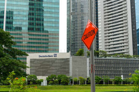 Singapore - September 16 2017: âCautionâ road sign next to Deutsche Bank sign in the office building in Central Business District in Singapore with no people in natural light, daytimeのeditorial素材