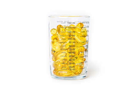 Bright yellow fish oil capsules in the glass measurement on white background shot with studio light