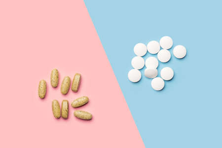 A pile of white pills and a pile of yellow vitamins on bright blue and pink background shot with studio light from aboveの写真素材