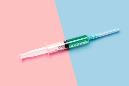 Large 10 ml plastic syringe with bright green liquid on bright pink and blue background shot with...