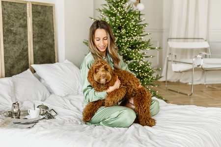 A Beautiful young woman with a golden brown labradoodle dog looking at the camera on Christmas tree,...
