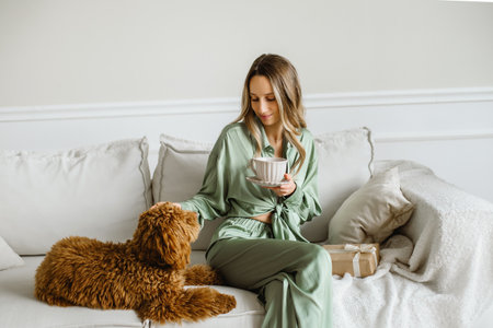 A Beautiful young woman with a golden brown labradoodle dog in living room at home, morning coffee. Cute Family puppy and girl play at home, decorated interior on holidays.の写真素材